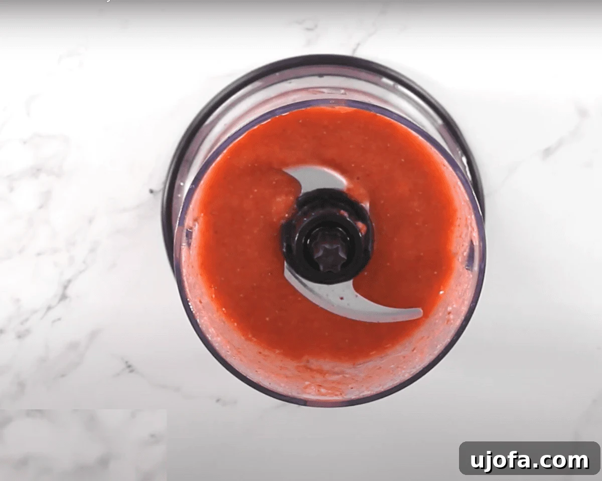 Luscious Strawberry Gluten-Free Cake 5 Overhead view of a food processor filled with smooth strawberry puree, sitting on a white marble countertop.