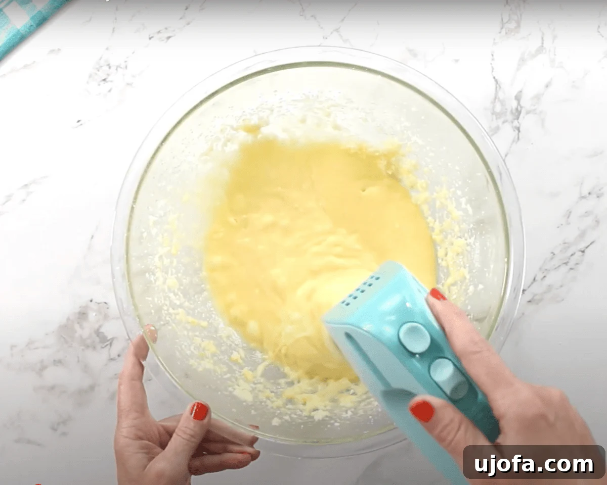 Luscious Strawberry Gluten-Free Cake 9 A glass mixing bowl with a smoother, yellow cake batter being mixed with a blue hand mixer.