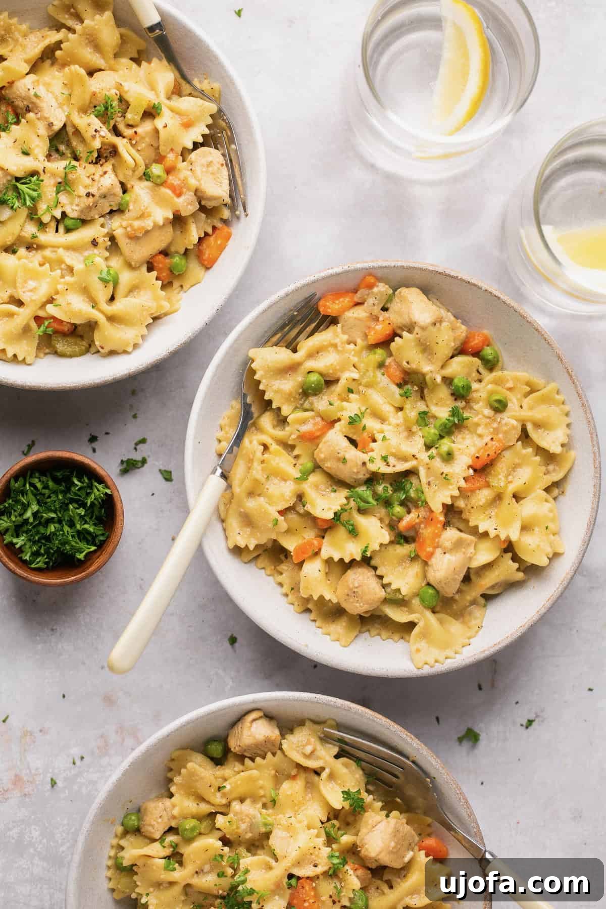 Three generous bowls of creamy Instant Pot chicken and gluten-free noodles, garnished with fresh herbs, with a fork resting on the side, ready to be served as a comforting family dinner.