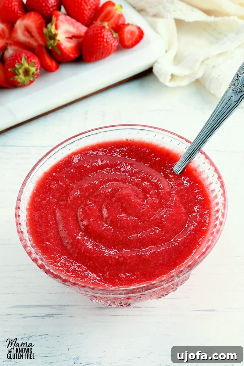 Luscious Strawberry Reduction 2 A glass bowl filled with rich, glossy strawberry reduction sauce, accompanied by a silver spoon. Fresh strawberries and a cream napkin are artfully arranged in the background, highlighting the sauce's natural ingredients.