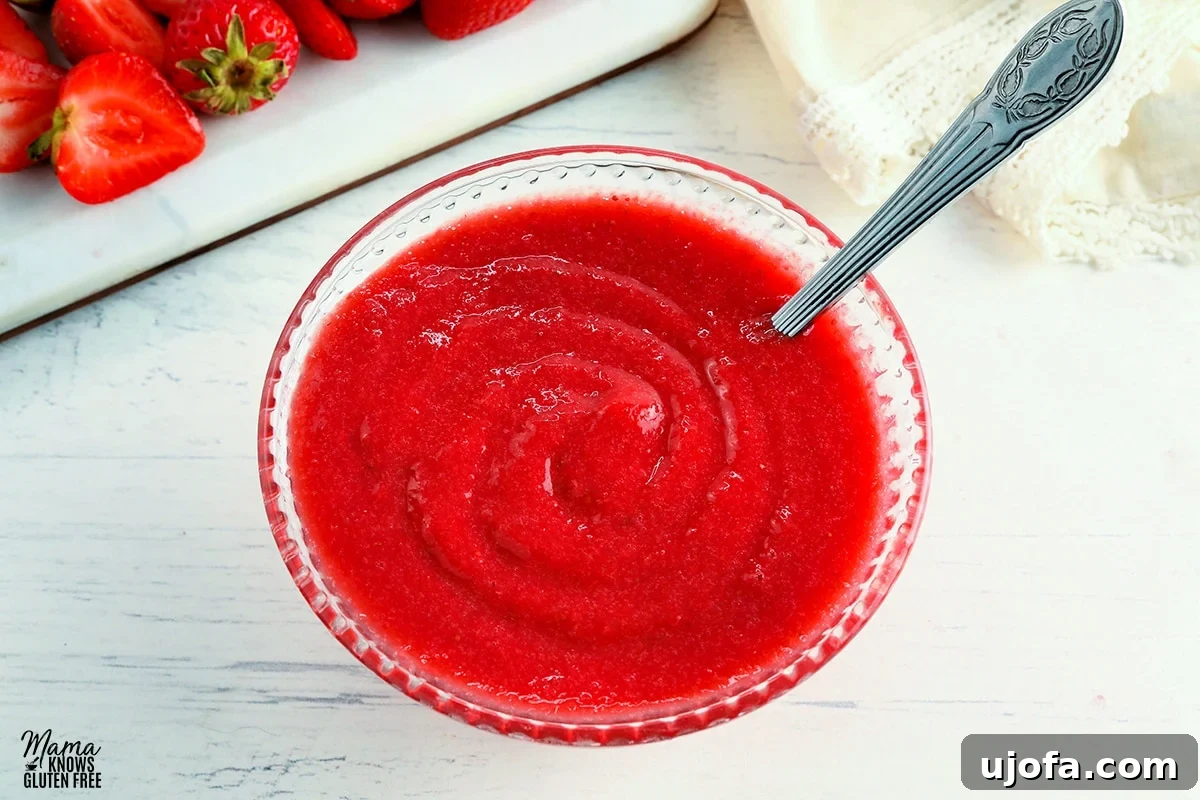 Luscious Strawberry Reduction 4 Close-up of strawberry reduction sauce in a clear glass bowl, with a spoon resting inside, showing its thick, glossy texture. Blurred fresh strawberries are visible in the background, creating a natural and inviting scene.