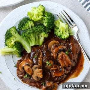 A plate of tender cube steak with homemade mushroom and onion gravy, alongside steamed broccoli.