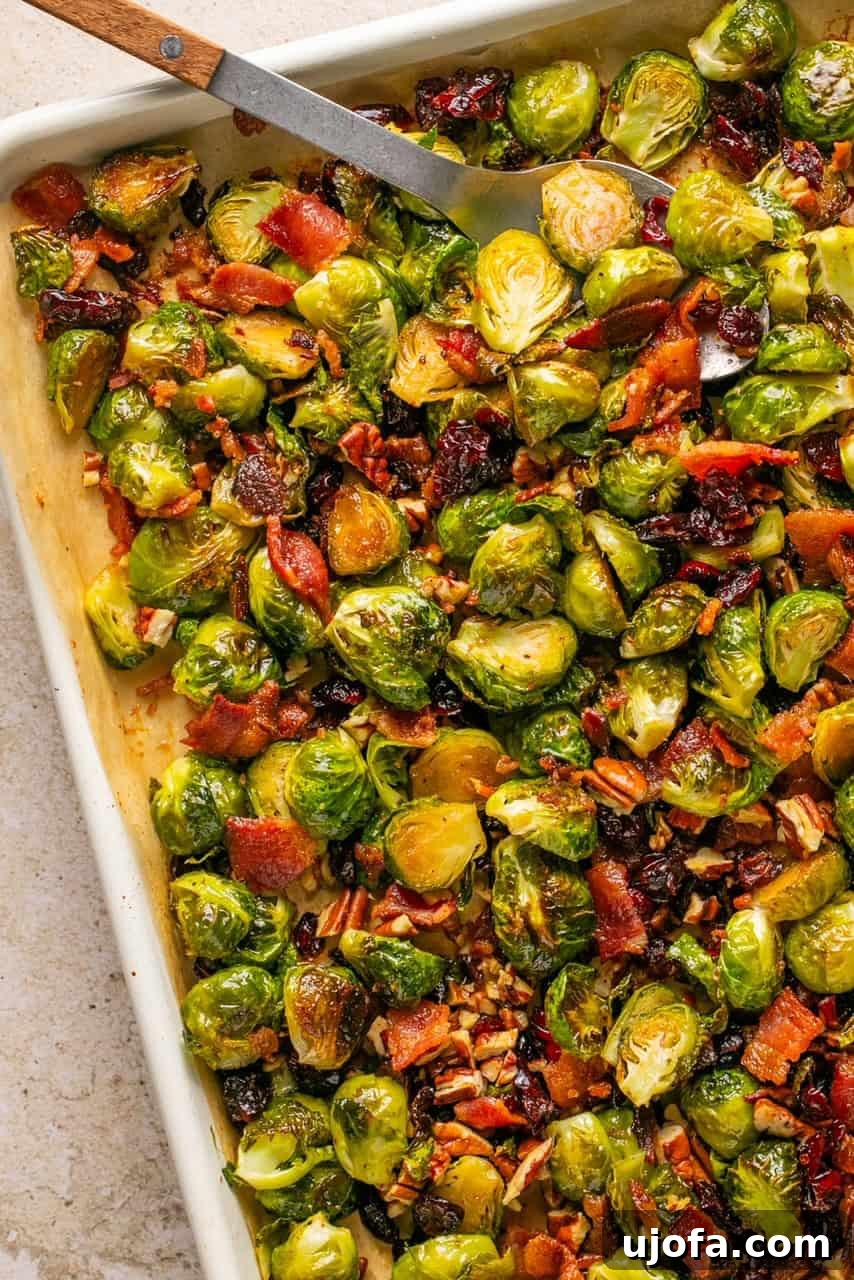 a spoon lifting maple bacon brussels sprouts off of a baking sheet