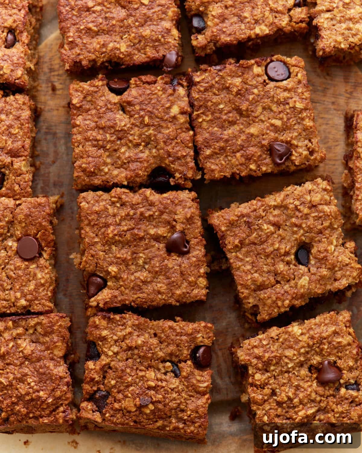 Close-up of sliced baked oatmeal bars with chocolate chips on a wooden surface, showing a golden-brown, chewy texture, ready to be enjoyed.