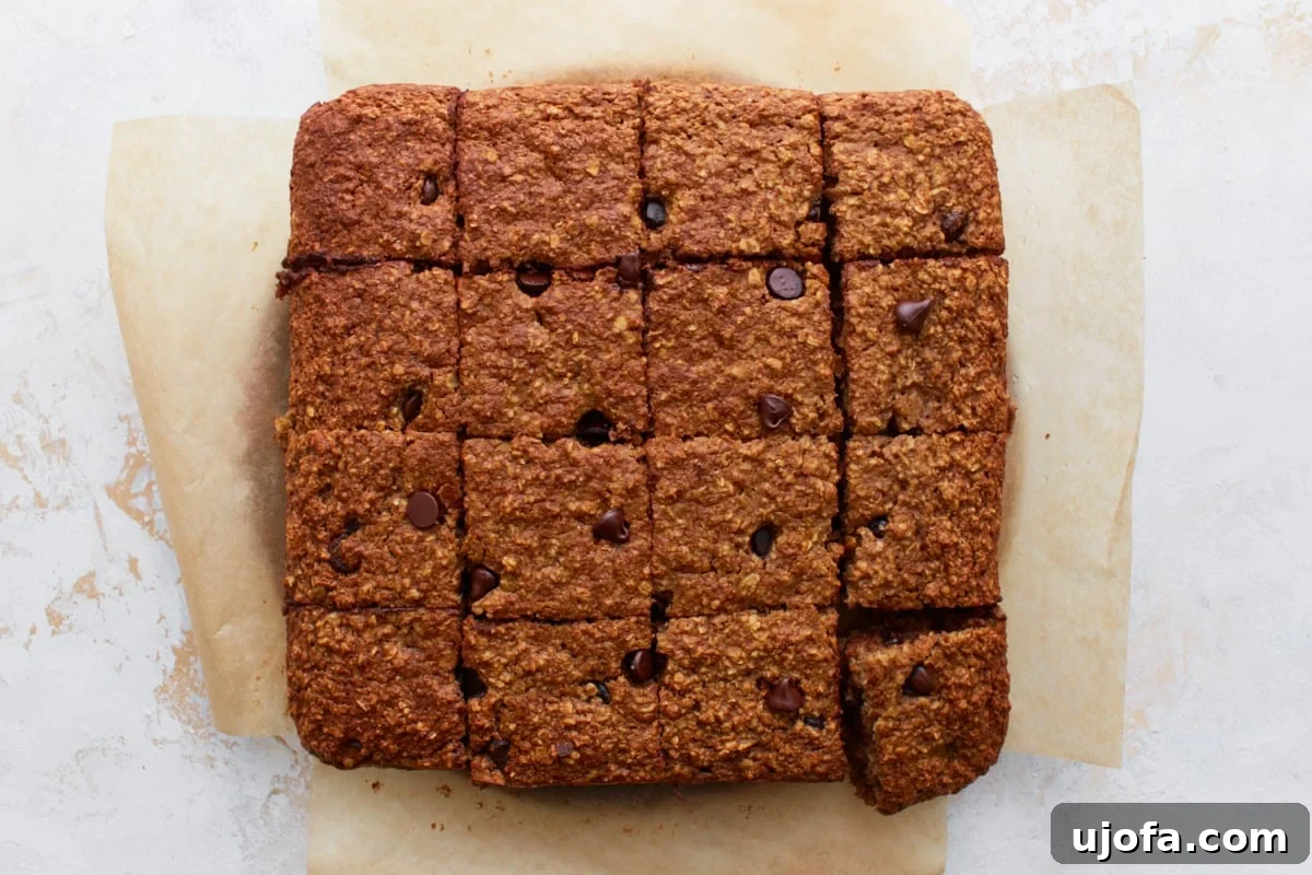 Baked oatmeal bars sliced into 16 even squares on parchment paper, ready to serve, displaying their soft and chewy texture.