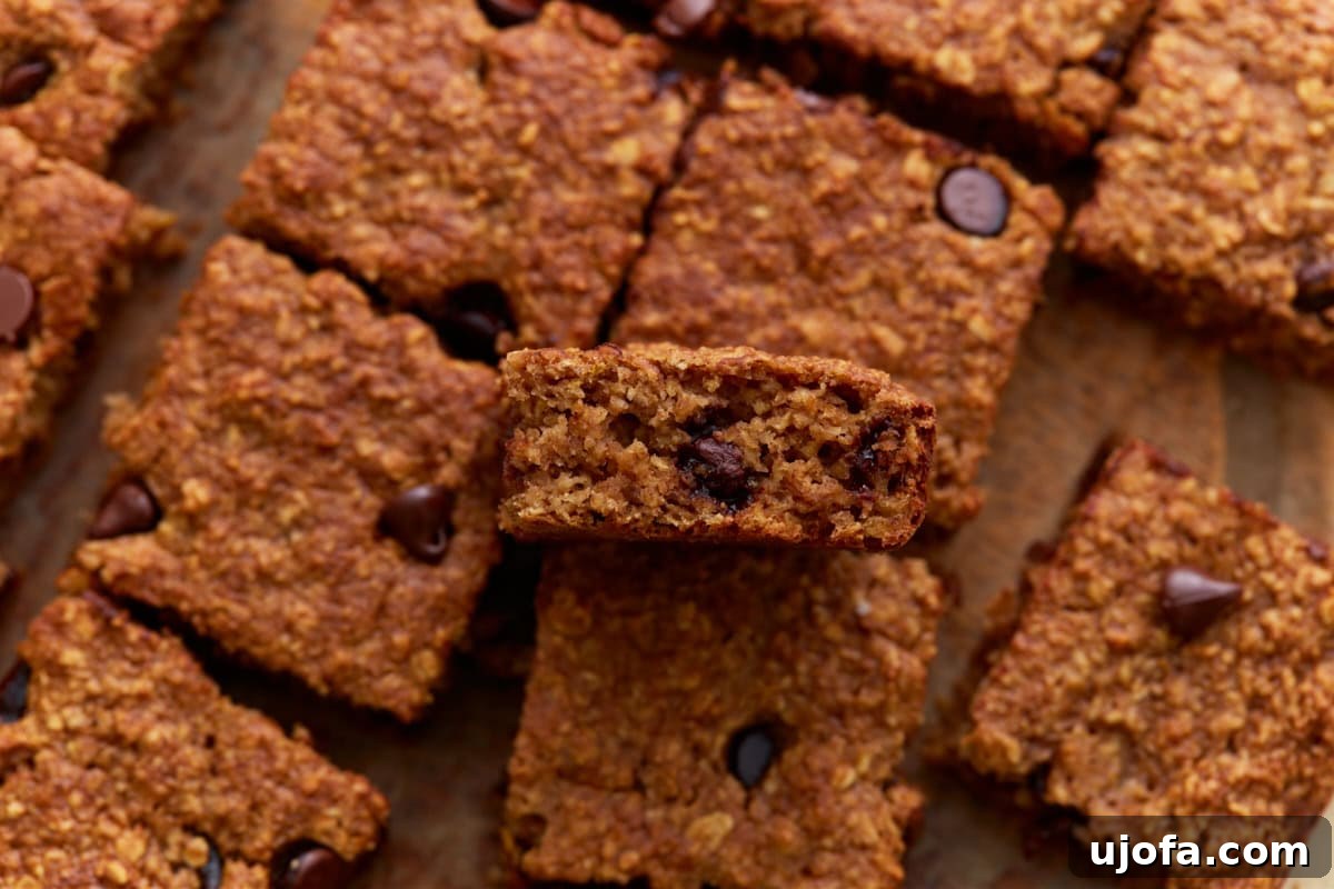 Close-up of a single oatmeal bar held above others, showing a moist, chewy interior with visible chocolate chips and a golden crust.