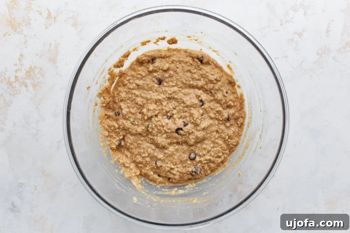 Oatmeal bar batter with chocolate chips stirred in, shown in a large glass bowl, ready for baking.