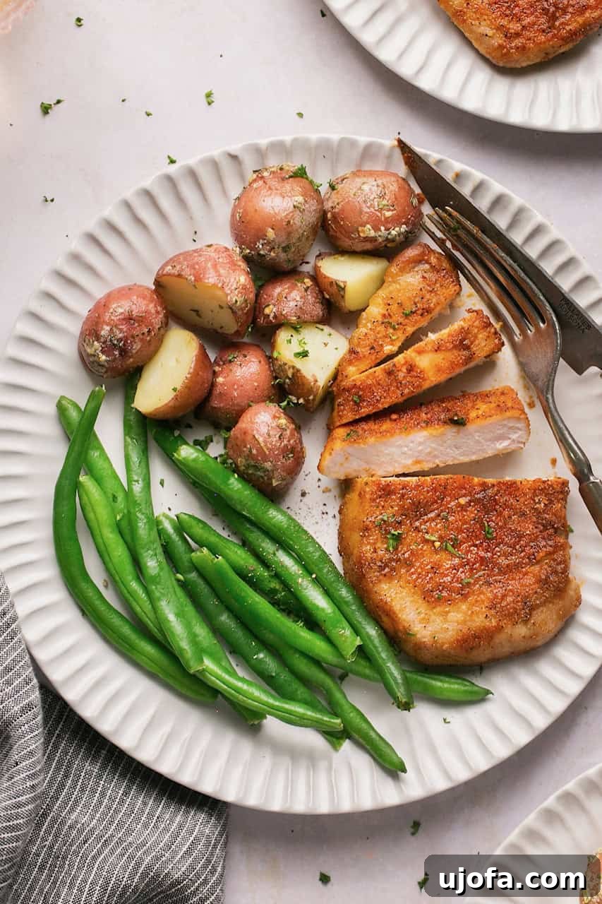 Crispy Air-Fried Pork Chops 2 A white plate with roasted potatoes, vibrant green beans, and two succulent air-fried pork chops, with a fork and knife elegantly resting beside it.