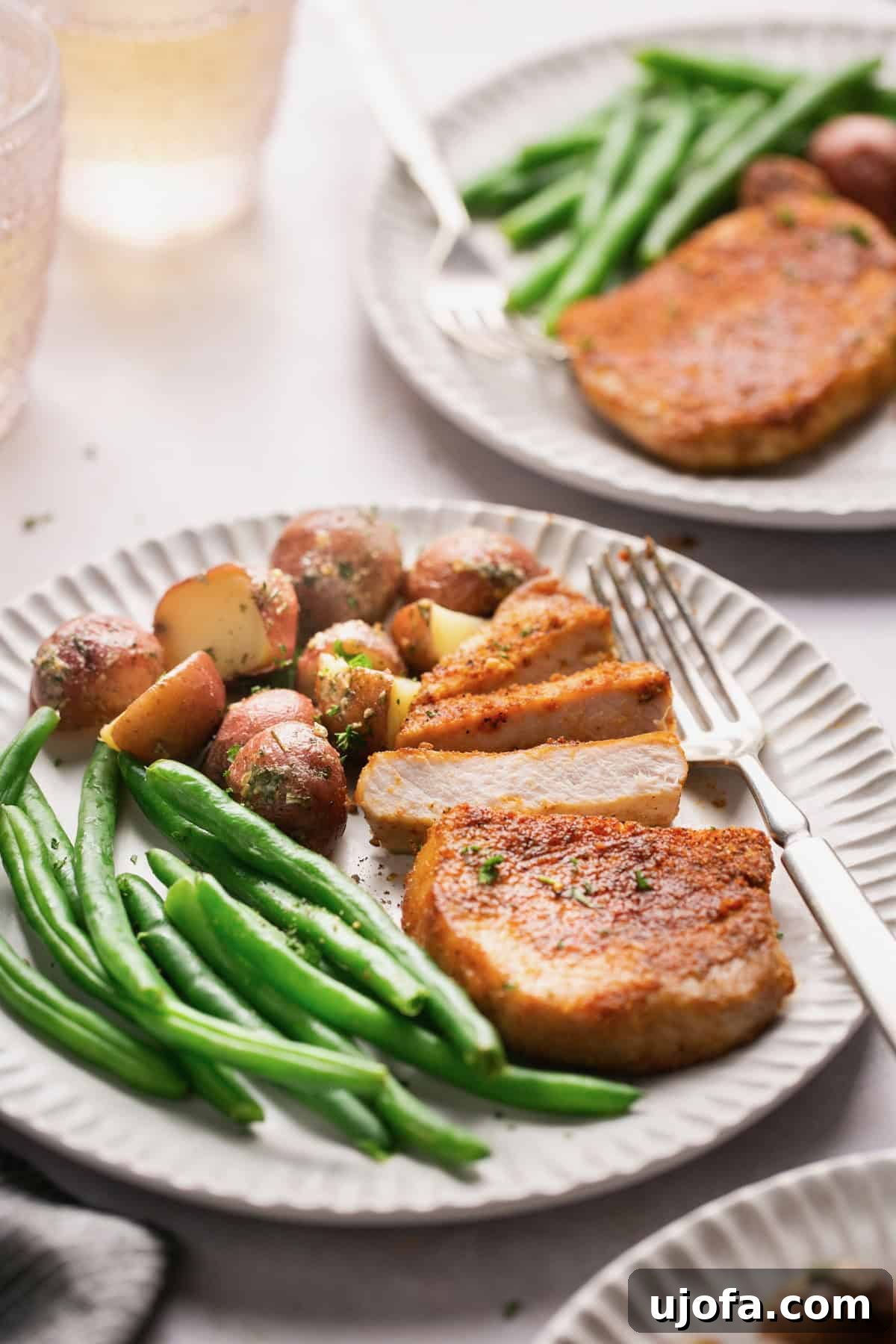 Crispy Air-Fried Pork Chops 7 Three white plates, each with a serving of roasted potatoes, green beans, and tender slices of pork chop.