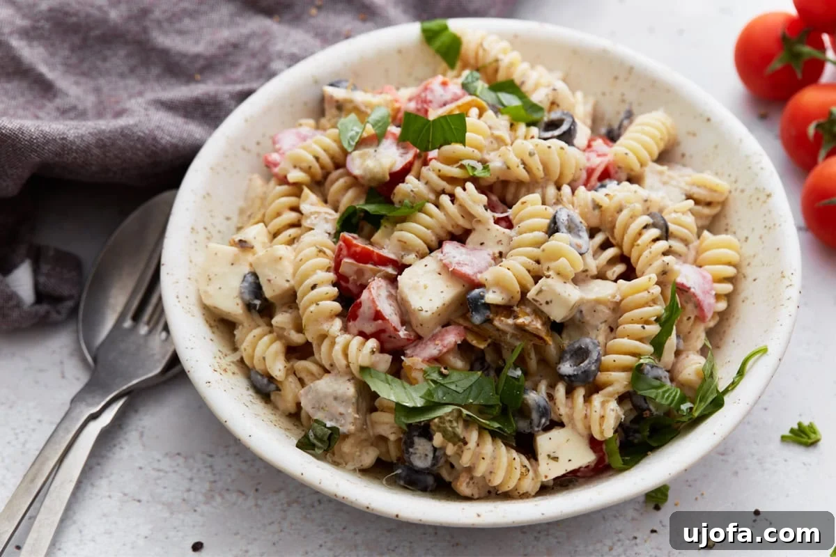 A detailed side view of a bountiful bowl of creamy Italian pasta salad, artfully arranged with a fork and spoon nearby, highlighting the enticing texture and vibrant, colorful ingredients.
