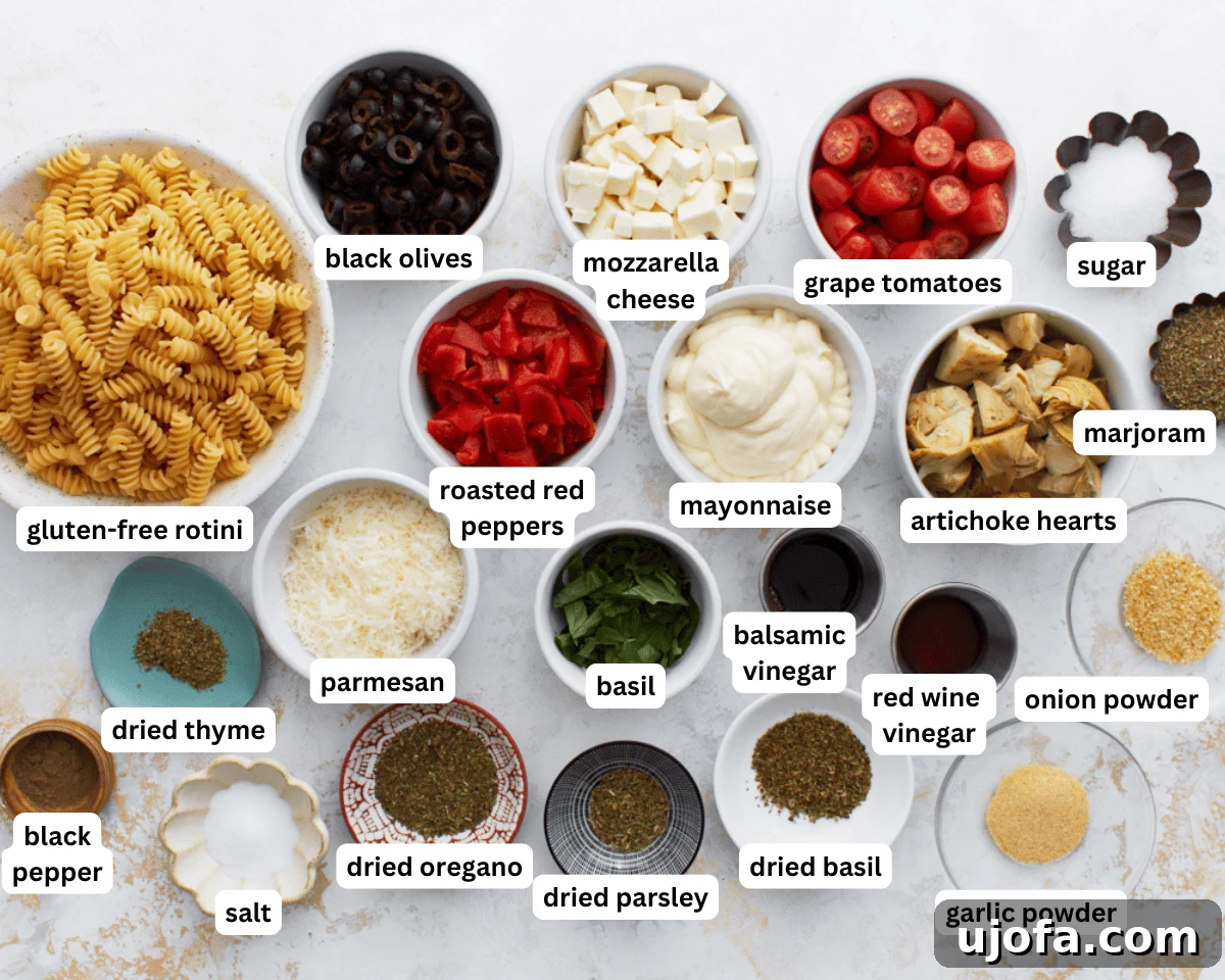 A collection of fresh, colorful ingredients for creamy Italian pasta salad laid out on a clean white surface, including gluten-free rotini pasta, various vegetables, and dressing components.