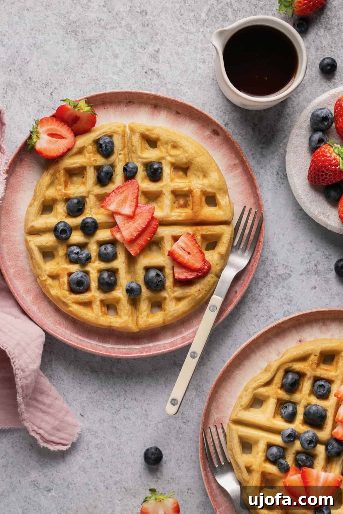 A gluten-free waffle on a pink plate topped with fresh blueberries and sliced strawberries, ready to be enjoyed.