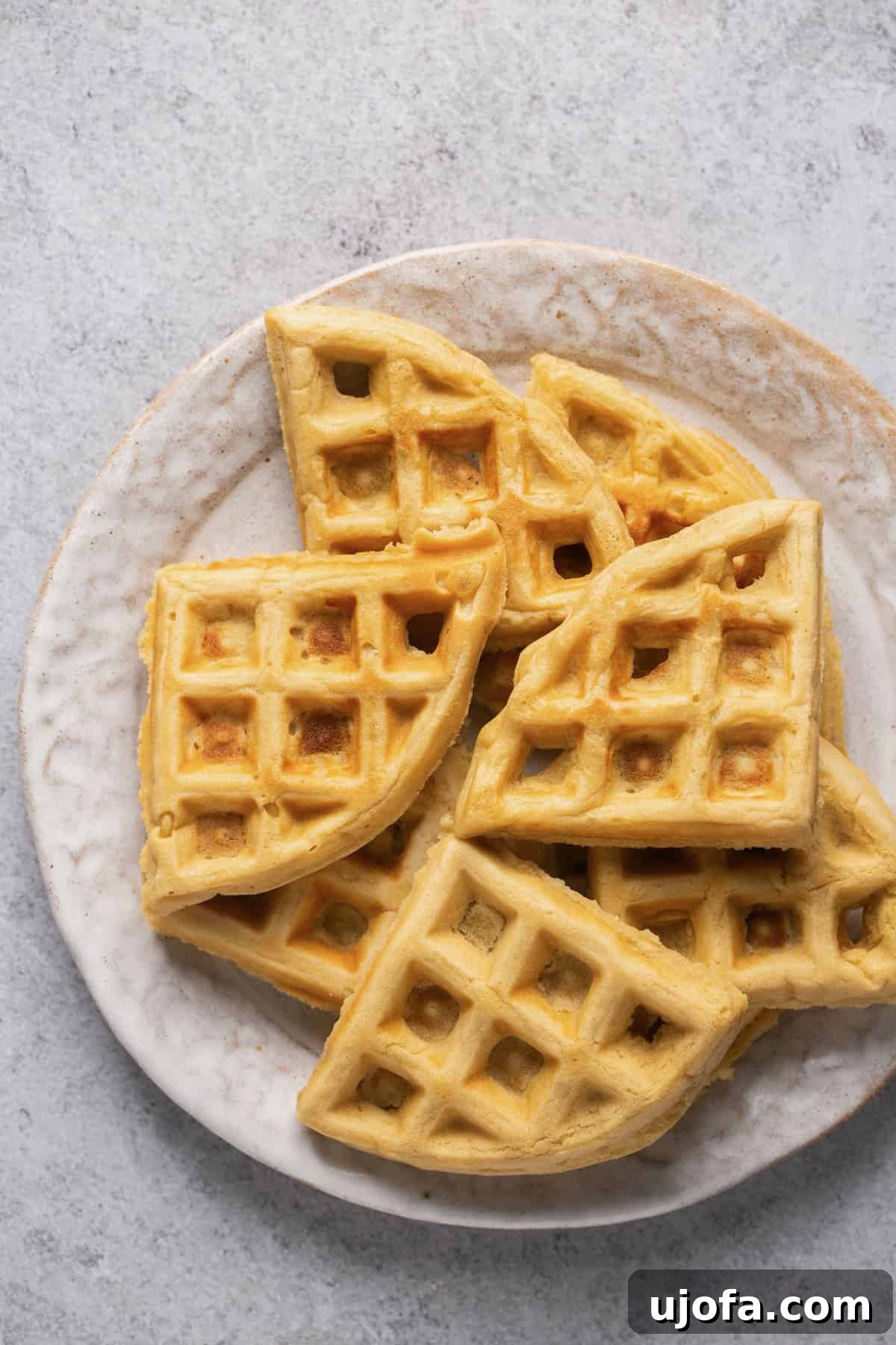 A stack of perfectly cooked gluten-free waffle triangles arranged on a white plate, showcasing their fluffy texture.