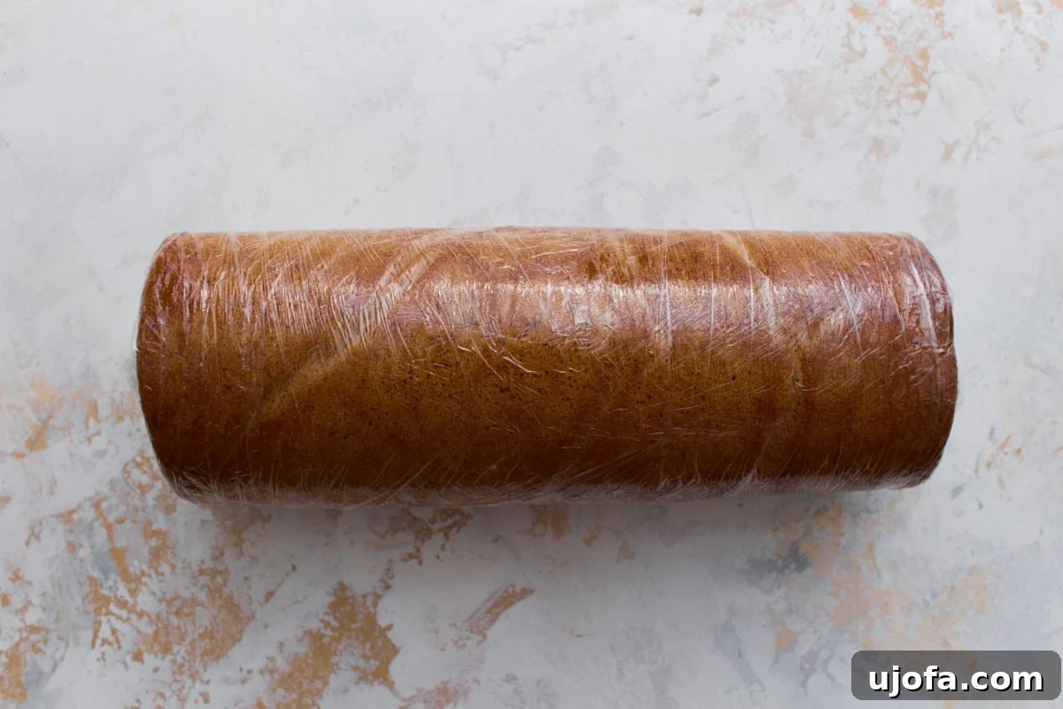 Gluten-free pumpkin roll tightly wrapped in plastic wrap, ready to chill in the refrigerator.