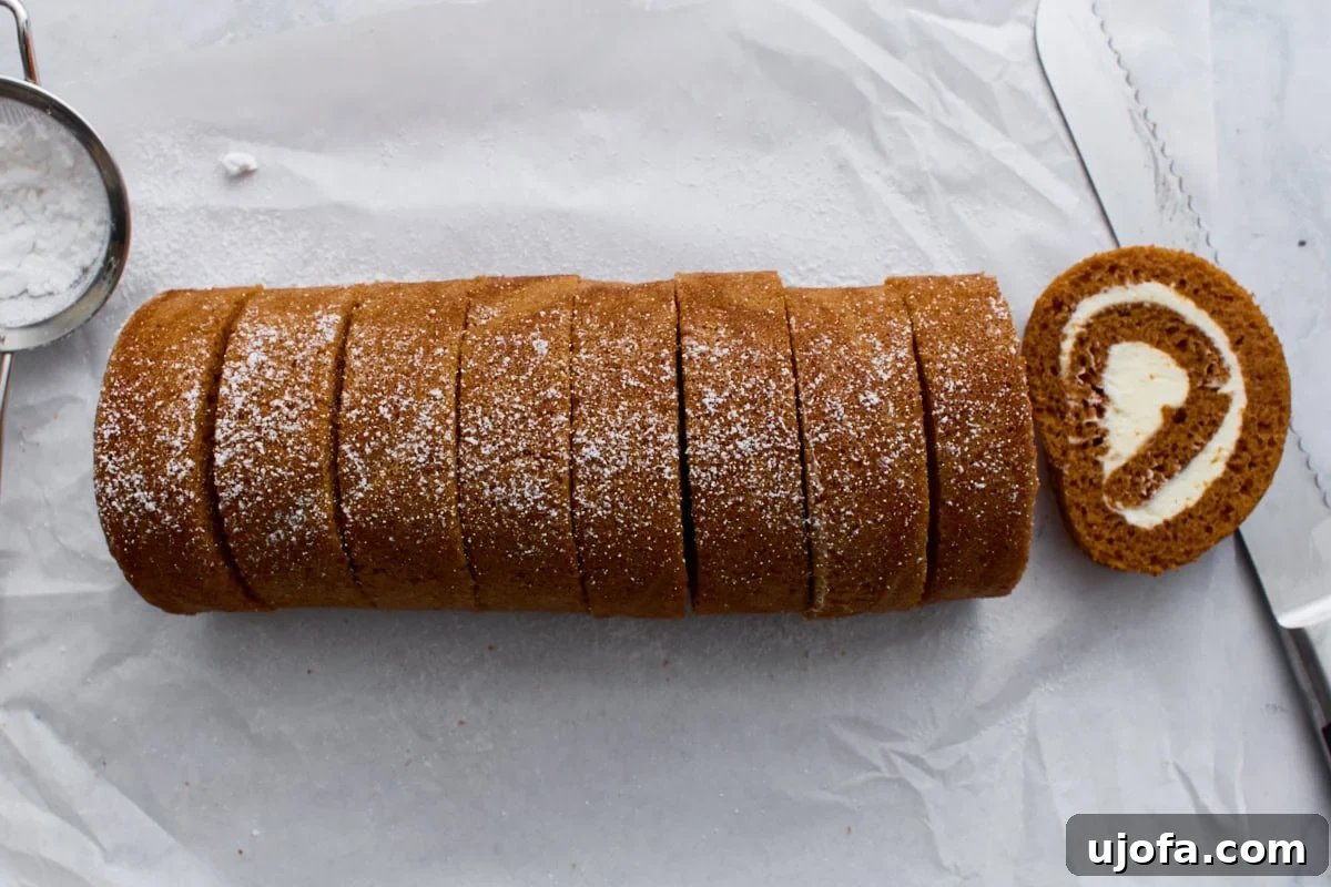Pumpkin roll dusted with powdered sugar and sliced into even pieces, showing the cream cheese swirl inside.