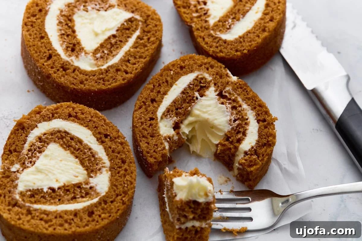 Close-up of pumpkin roll slices on parchment paper with one piece cut into by a fork, highlighting the creamy filling.
