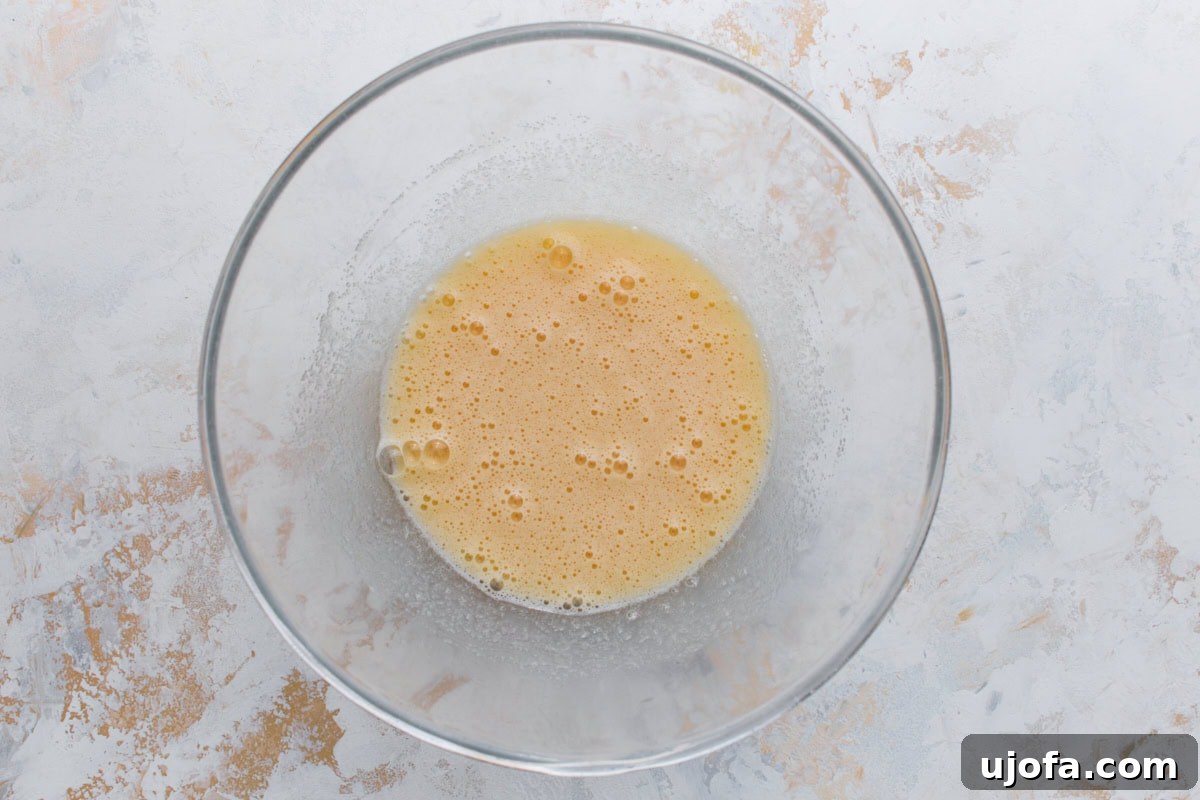 Glass bowl with beaten eggs and sugar mixture, pale yellow and slightly frothy.