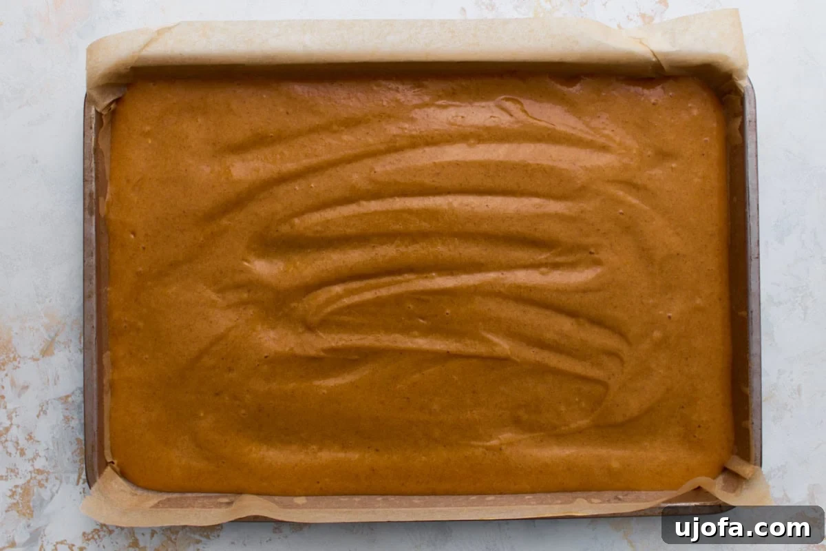 Pumpkin roll batter spread evenly into a parchment-lined jelly roll pan, ready to bake.
