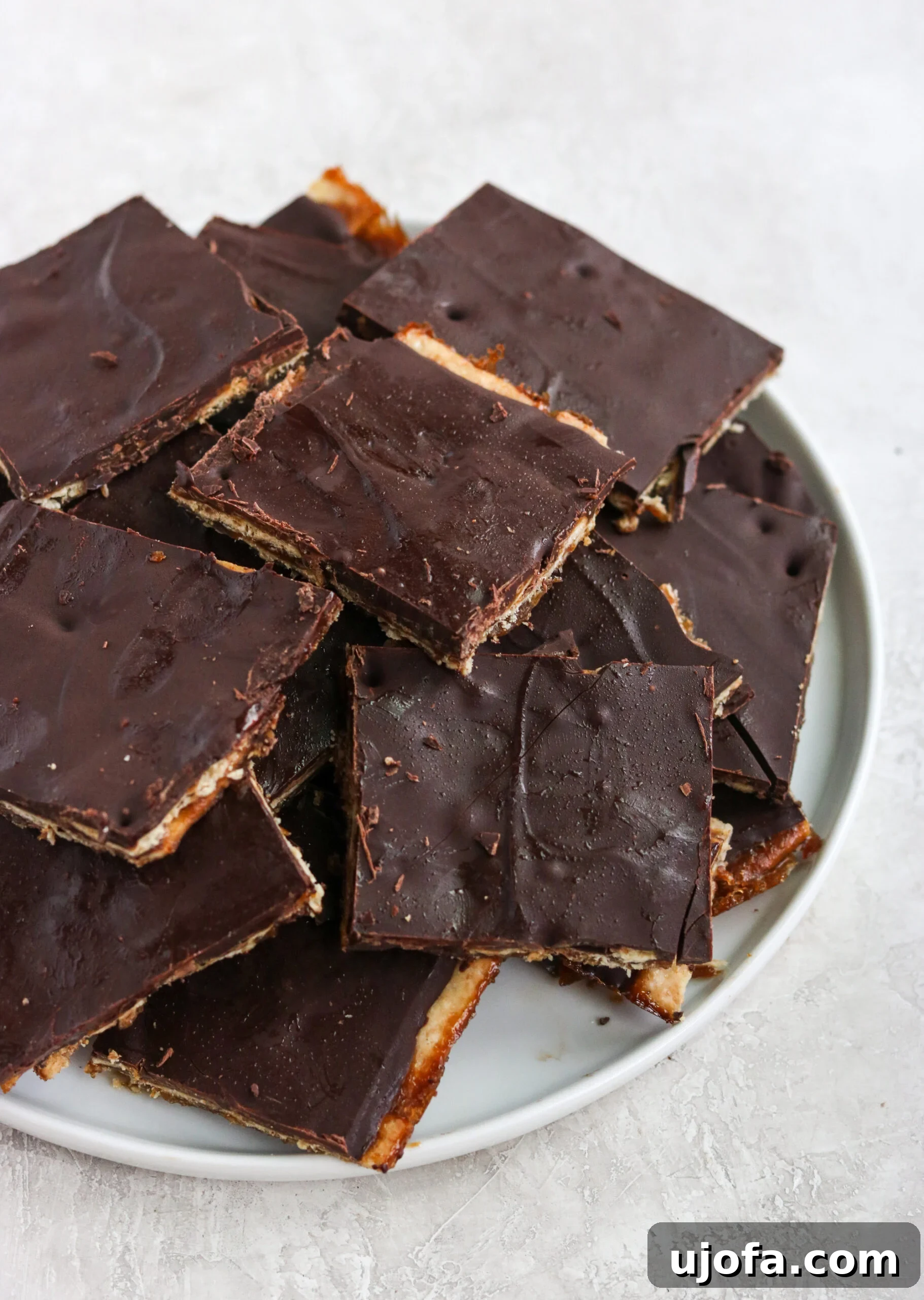 A close-up of Christmas crack dessert bars arranged on a white plate, showcasing the distinct layers of cracker, caramel, and chocolate, ready to be enjoyed.