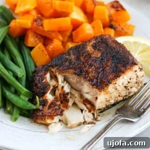 A perfectly cooked blackened mahi mahi fillet on a plate, served with roasted butternut squash and crisp green beans. A fork gently flakes the tender fish.