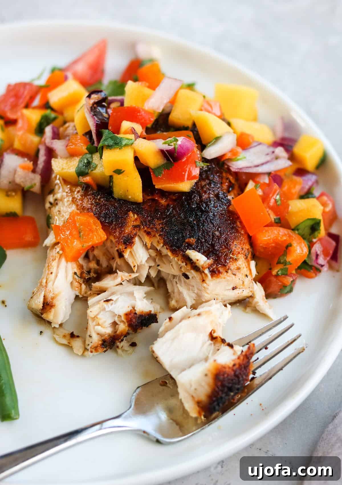 A glistening blackened fish fillet generously topped with a vibrant, fresh mango salsa, creating a beautiful contrast of colors and flavors.