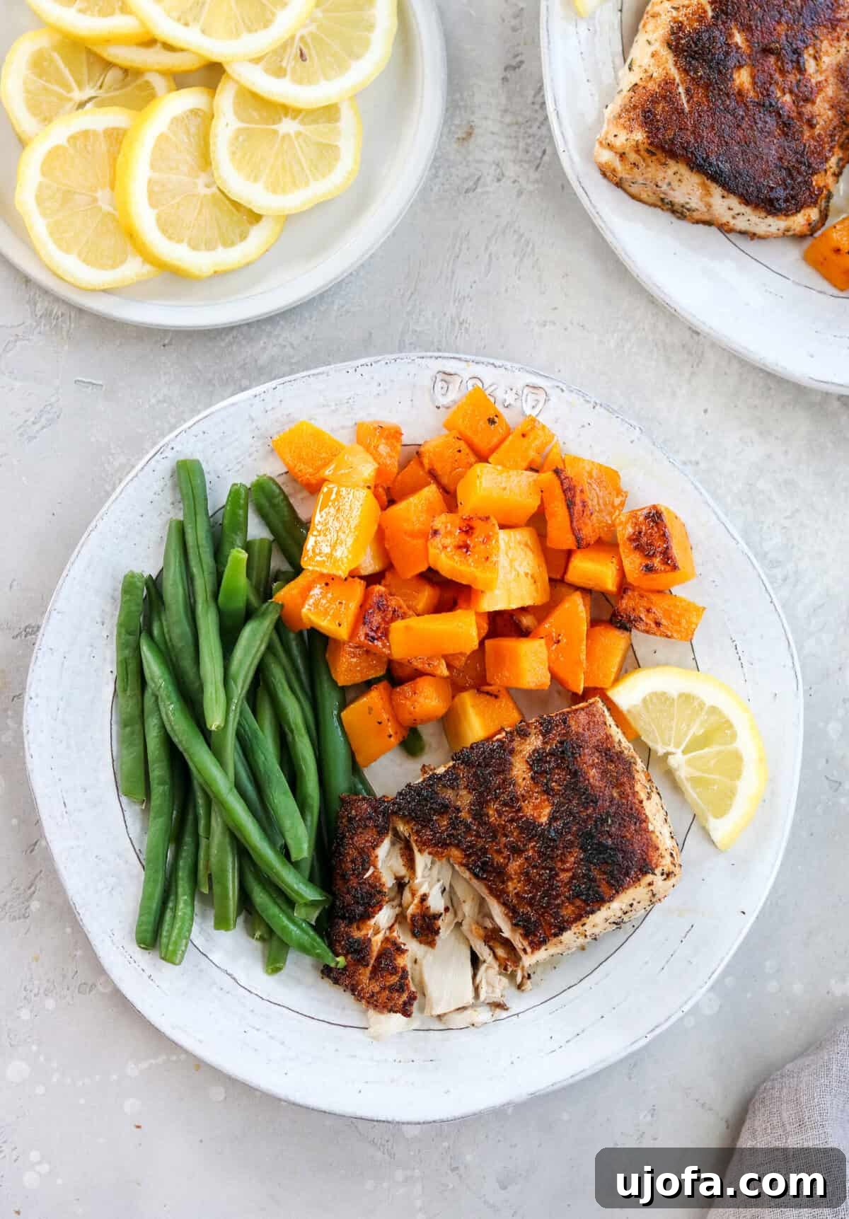 An overhead shot of a white plate generously filled with a balanced meal: vibrant green beans, golden sweet potatoes, and tender white fish.