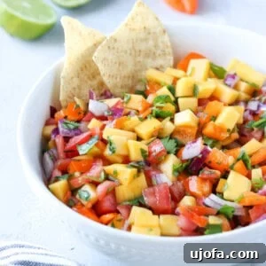mango habanero salsa in a bowl with 2 chips sticking out with limes and a habanero in the background