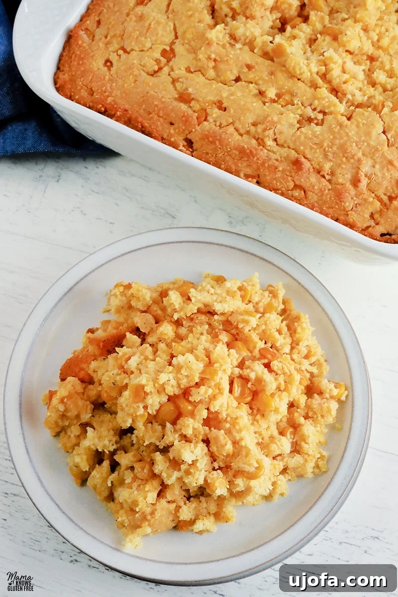 Gluten-free corn casserole serving on a white plate with the casserole in the background, highlighting its golden-brown top and moist interior.