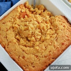 Gluten-free corn casserole in a white baking dish with a serving spoon, showcasing its rich, golden texture.