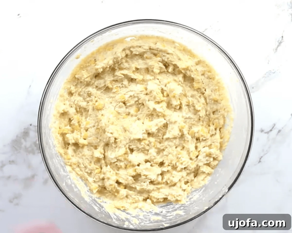 Thick gluten-free corn casserole batter mixed with creamed corn and whole kernel corn in a clear glass bowl.