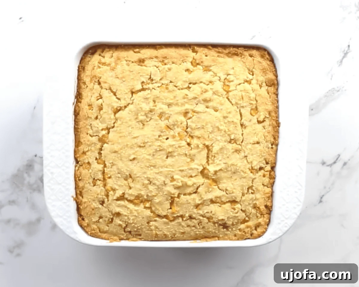 Golden baked gluten-free corn casserole in a square white dish with a lightly cracked, set top.