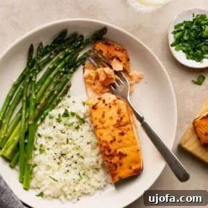 Effortless Air Fryer Salmon Straight From Frozen 8 Air fryer frozen salmon with honey garlic sauce and cauliflower rice and asparagus in a bowl with a fork flaking the fish
