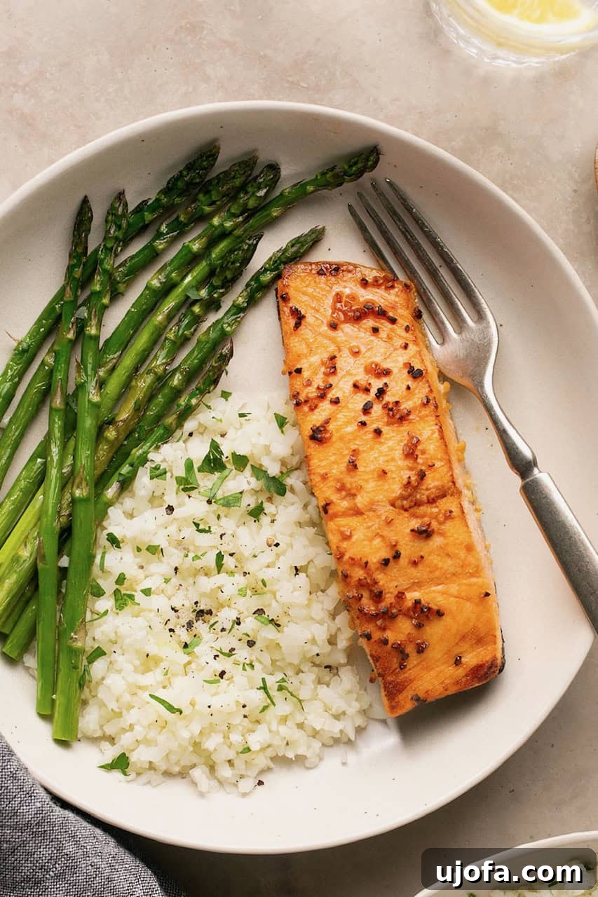 Effortless Air Fryer Salmon Straight From Frozen 6 A single piece of flaky air fryer salmon on a plate, elegantly accompanied by white rice and vibrant green asparagus spears.