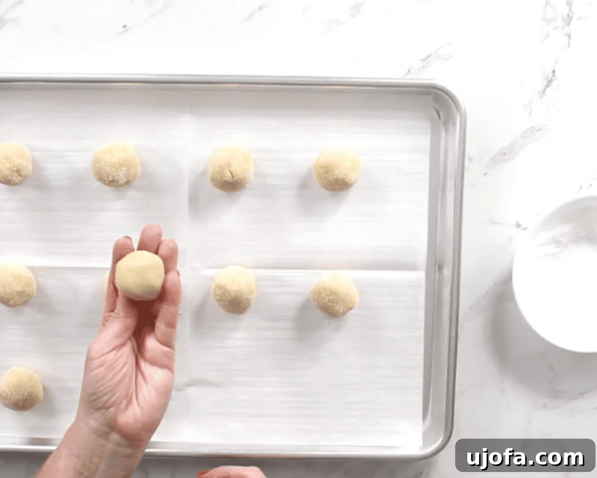 rolling gluten-free thumbprint cookies on a cookie sheet 