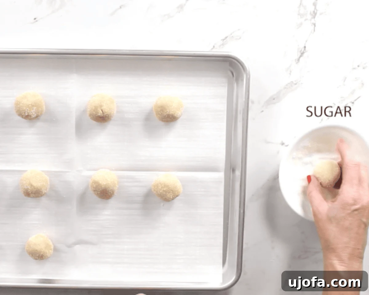 gluten-free thumbprint cookie dough balls being shaped on a cookie sheet