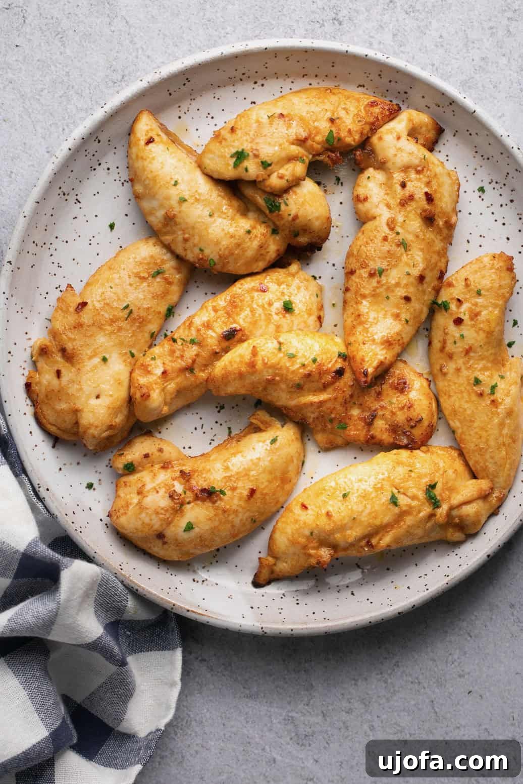 Nine golden air fryer chicken tenderloins arranged on a white speckled plate, ready to be served.