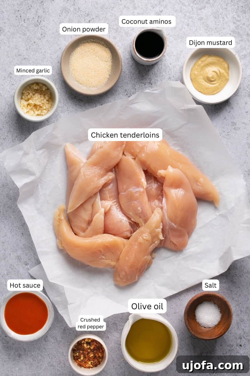Individual bowls of ingredients for air fryer chicken tenderloins, neatly arranged for easy preparation, alongside raw chicken tenderloins on parchment paper.