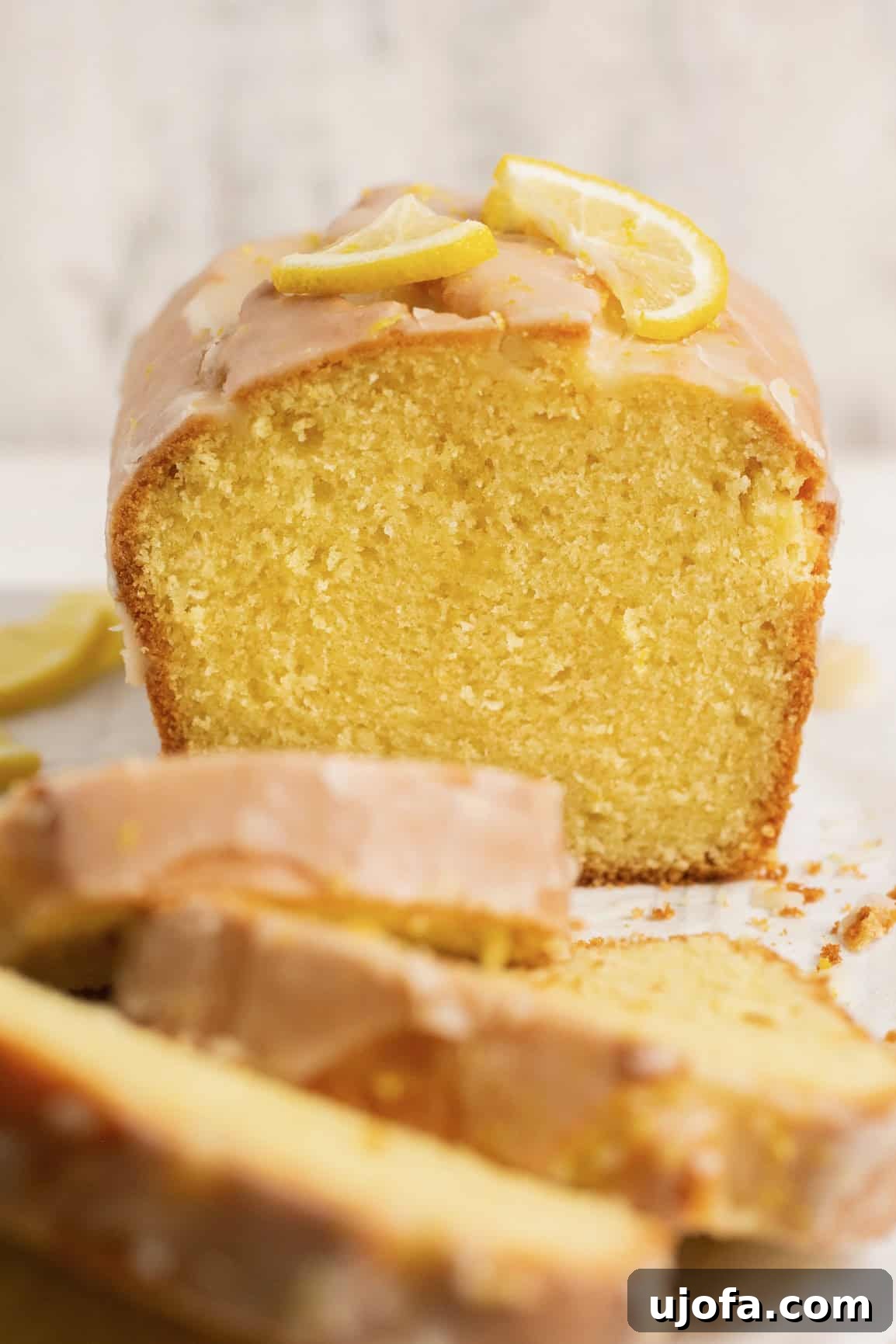 Zesty Gluten-Free Lemon Drizzle Cake 2 gluten free lemon drizzle cake on parchment paper with the loaf in the background and 3 slices in front