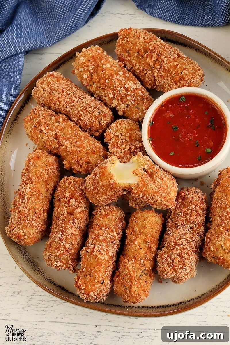 Guilt Free Mozzarella Sticks 2 Crispy gluten-free mozzarella sticks on a white plate with a side of marinara sauce for dipping.