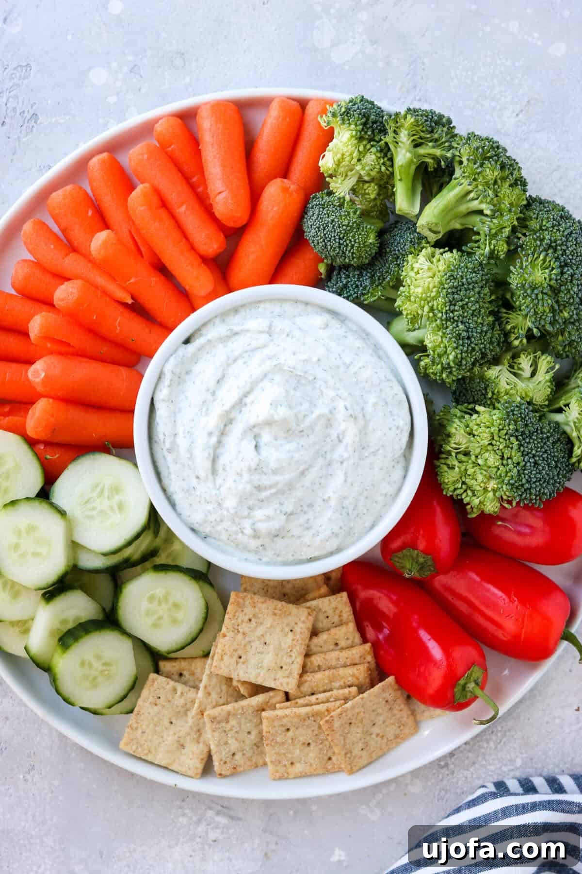 A vibrant platter of fresh vegetables and gluten-free crackers, with a small bowl of creamy cottage cheese ranch dip placed prominently in the center.