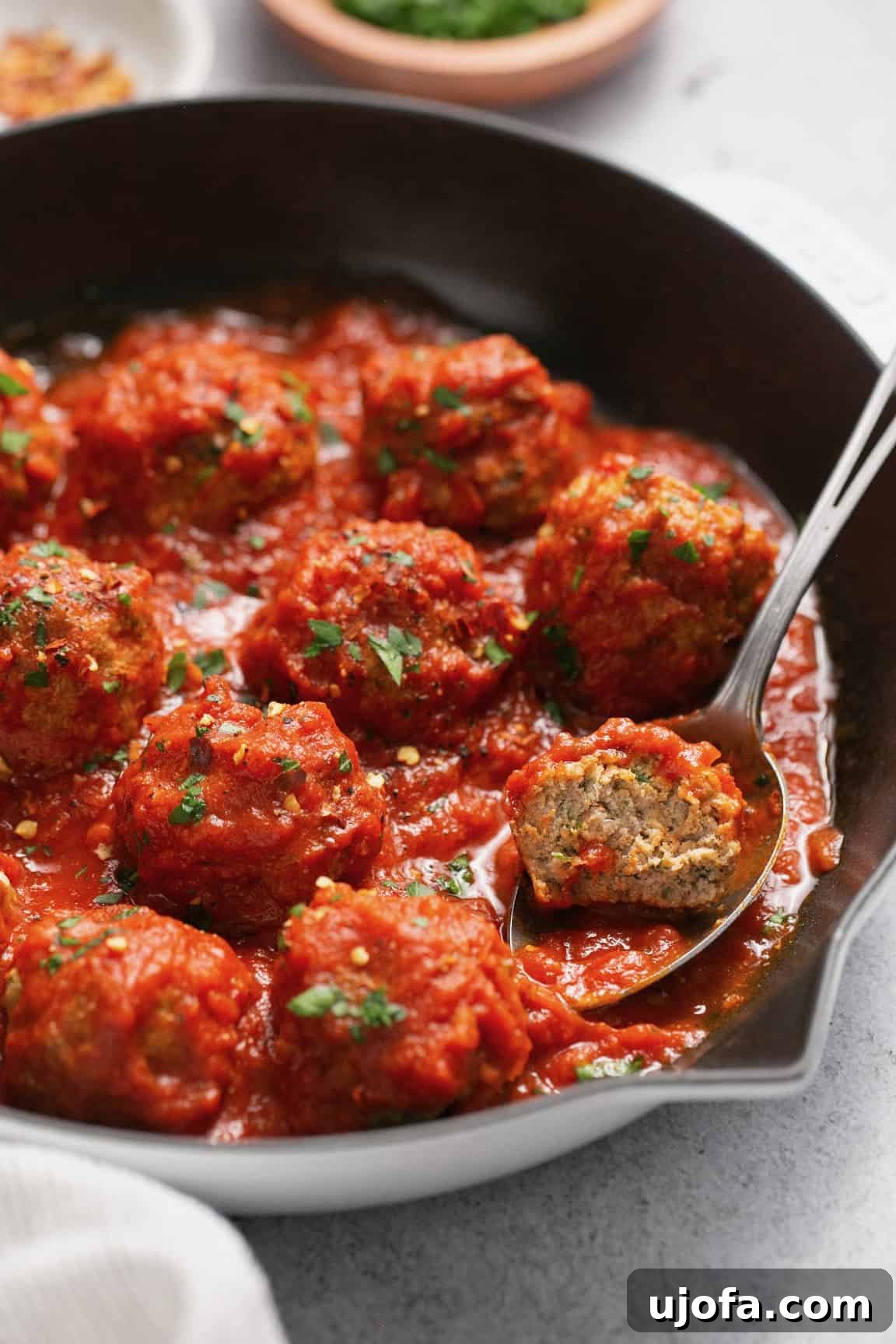 air fryer turkey meatballs in a cast iron skillet with marinara sauce and a spoon scooping one out