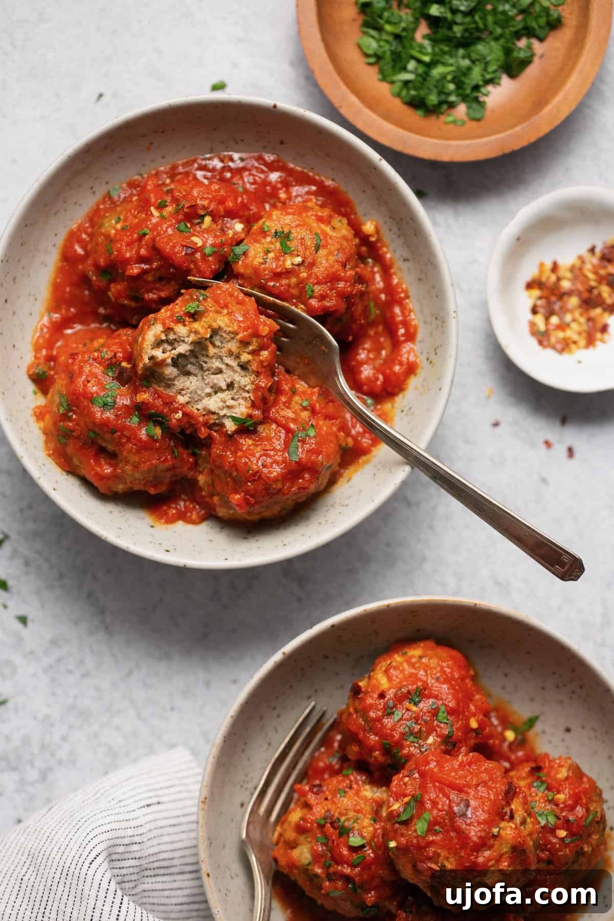 gluten free meatballs with sauce in two bowls with a spoon and parsley and crushed red pepper on the side