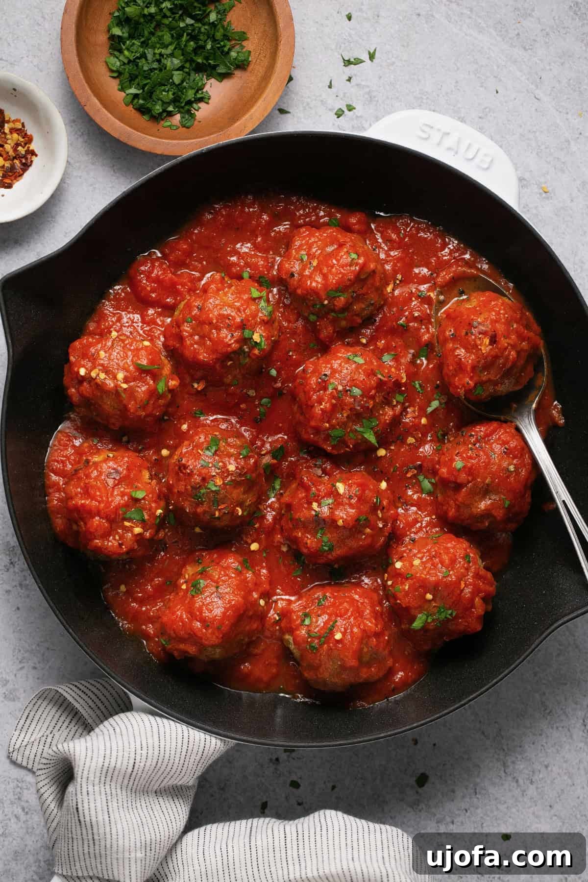 gluten free meatballs with sauce in a white and black cast iron skillet topped with parsley