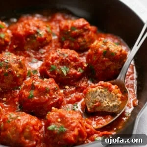 air fryer turkey meatballs in a cast iron skillet with marinara sauce and a spoon scooping one out