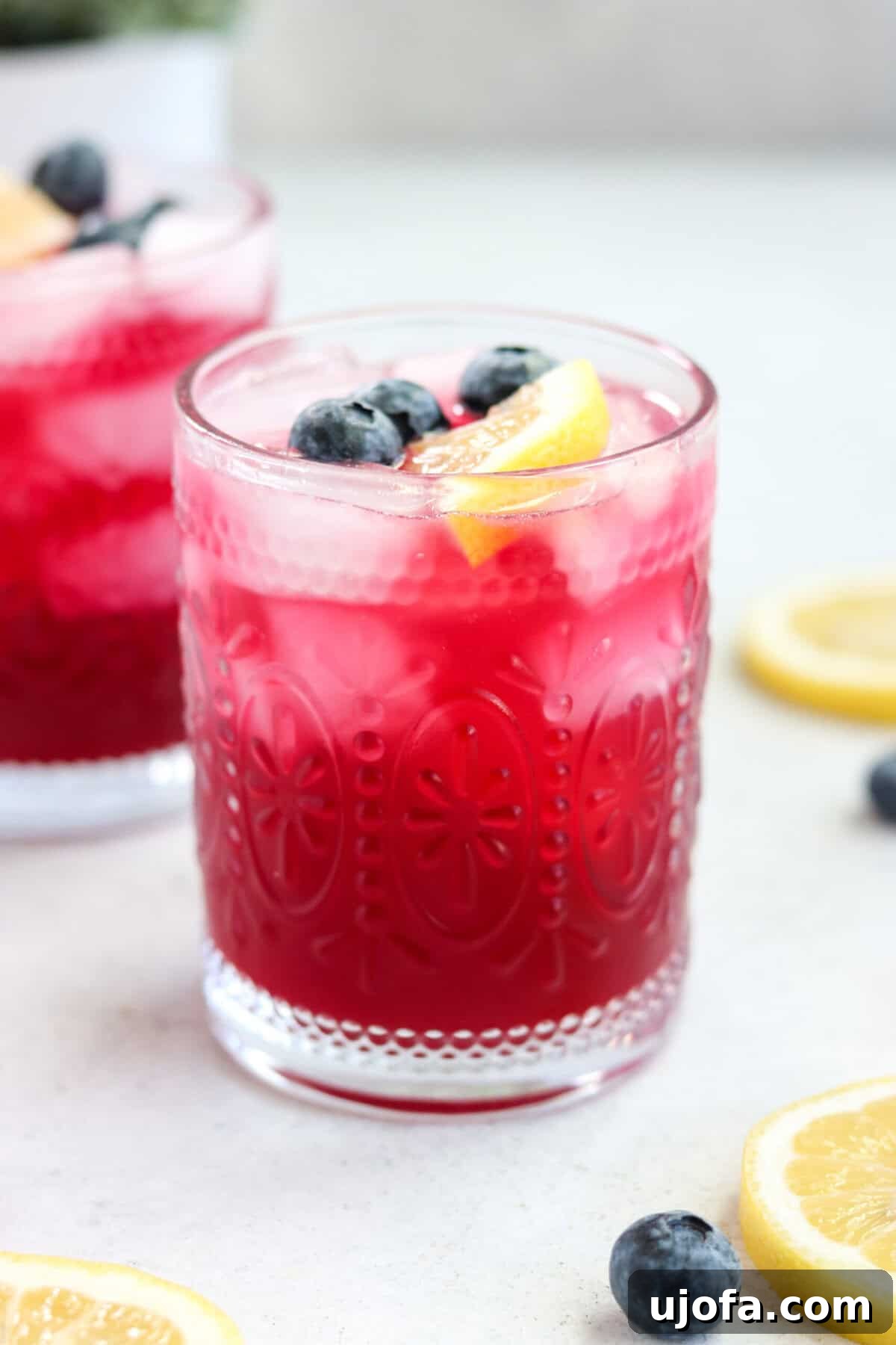An up-close photo of a vibrant lemon blueberry mocktail in a clear glass, beautifully garnished with fresh blueberries and a lemon slice.