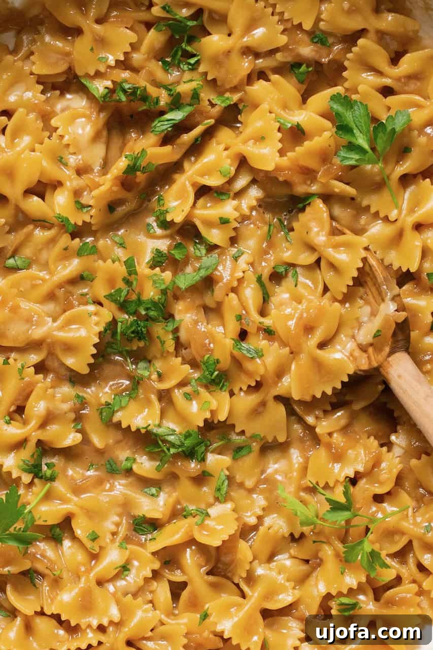 TikTok's Must-Try Gluten-Free French Onion Pasta 6 An inviting close-up of cooked French onion pasta being stirred with a wooden spoon in a pot, showcasing its creamy texture.