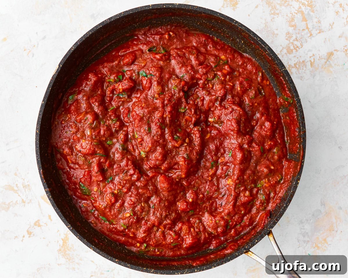 Grated Parmesan cheese and fresh green herbs being stirred into the simmering gluten-free spaghetti sauce, adding final touches.