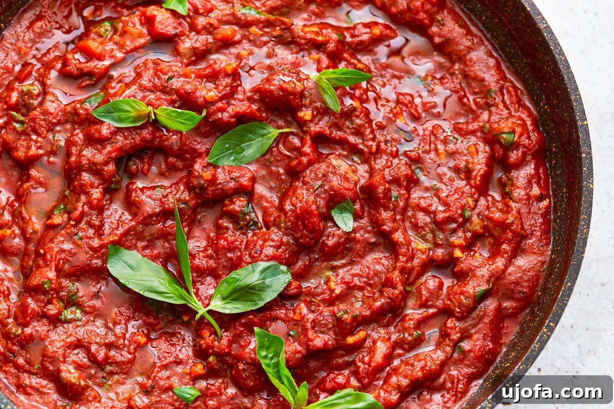 A close-up view of rich gluten-free spaghetti sauce simmering in a skillet, garnished with fresh basil leaves.