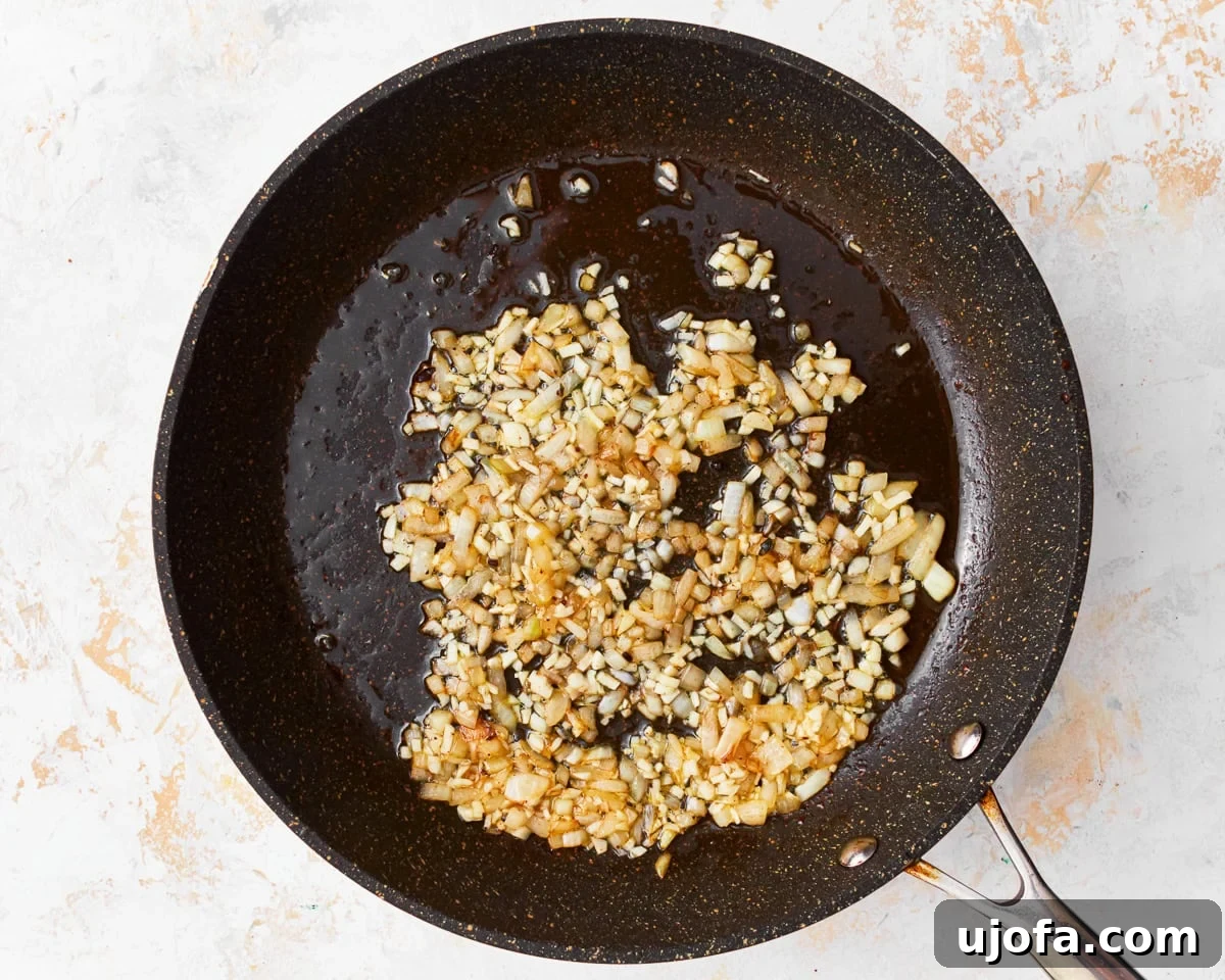 Finely chopped garlic and onion cooking gently in olive oil within a skillet, releasing their fragrant aromas.
