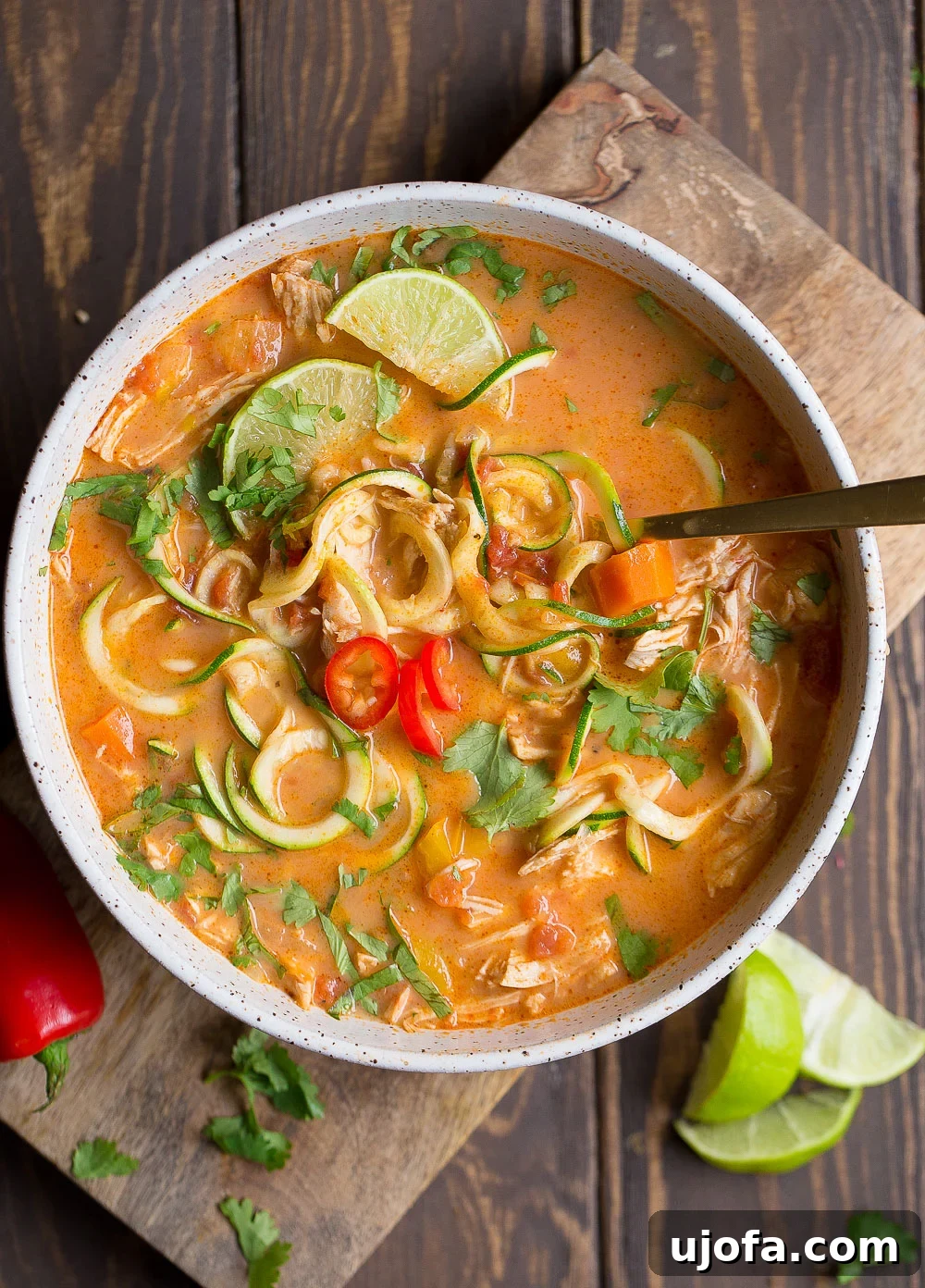 An aromatic bowl of Whole30 Thai Chicken Zoodle Soup, garnished with fresh cilantro and lime.